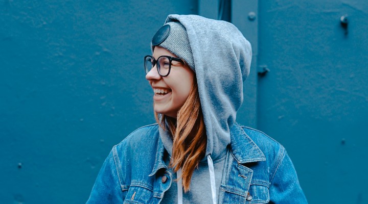 A woman with a blue hoodie on and glasses laughing.