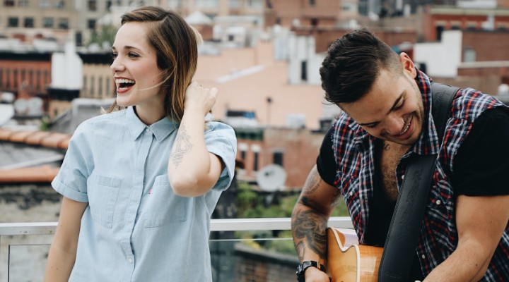 A young woman laughing and a man playing guitar on a rooftop.