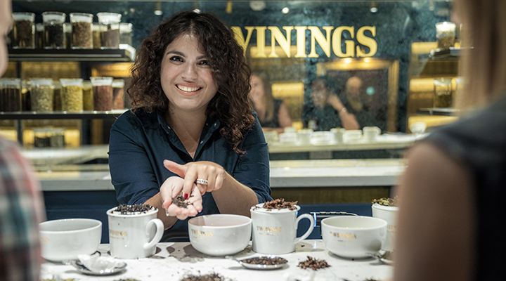 A friendly woman teaching a tea blending class at Twinings, holding a handful of tea.