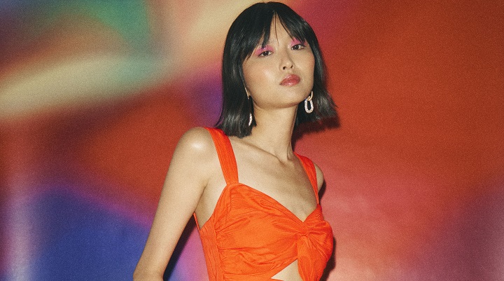 Asian model wearing bright orange dress against colourful backdrop