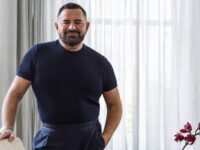 Mid shot of male Australian designer Steven Khalil in navy shirt and pants against neutral background in styled living room.