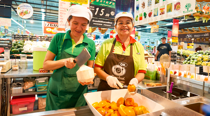 Two female employees are shown cutting up fresh fruit in a Big C hypermarket in Thailand.