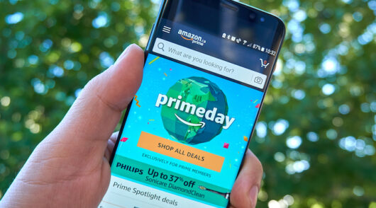 A man’s hand holding an iPhone, with the screen showcasing Amazon’s Prime Day homepage.