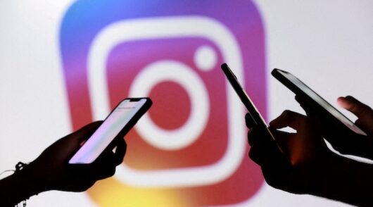 Teenagers pose for a photo while holding smartphones in front of a Facebook logo in this illustration