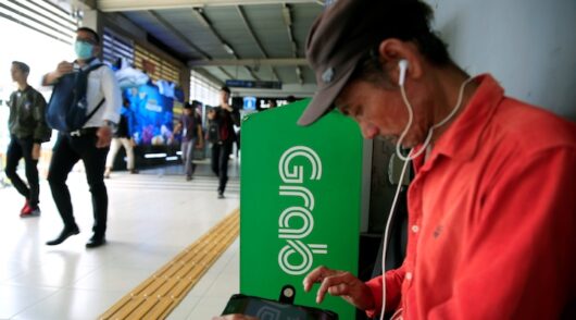 A passenger sits next to Grab corner sign as he waits for a Grab bike at Sudirman train station in Jakarta, Indonesia