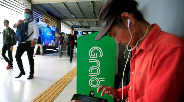 A passenger sits next to Grab corner sign as he waits for a Grab bike at Sudirman train station in Jakarta, Indonesia
