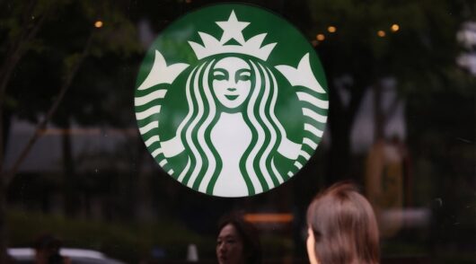 A woman walks past a logo of Starbucks in Seoul